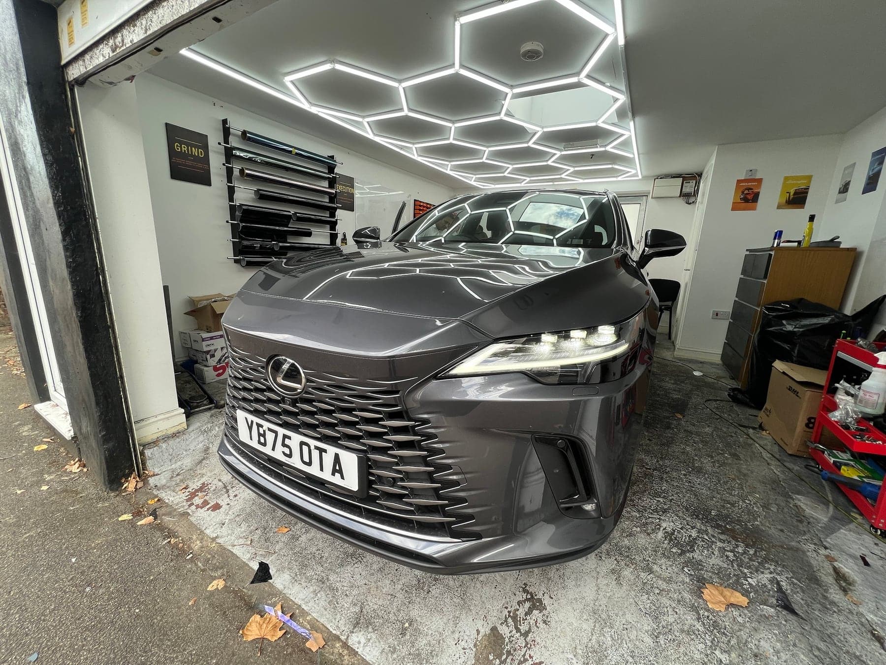 Lexus RX with tinted windows inside the Executive Tints & Repairs unit in Walthamstow, seen from the roller shutter with hexagon lighting overhead